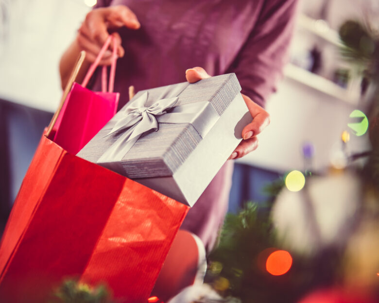 Woman standing by the christmas tree and taking a christmas present out of shopping bag