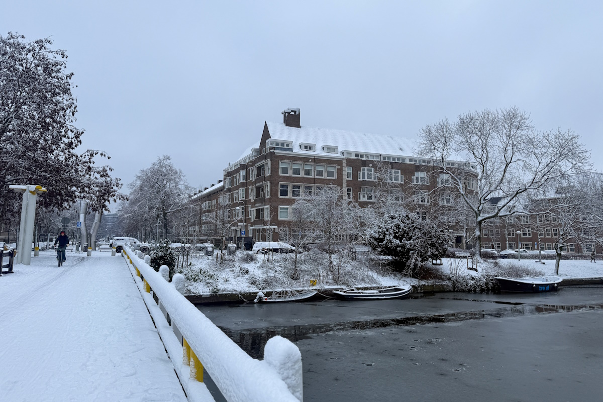 Ένα άτομο κάνει ποδήλατο στο χιόνι, σε μια γέφυρα πάνω από ένα ποτάμι καλυμμένο με πάγο στο Άμστερνταμ