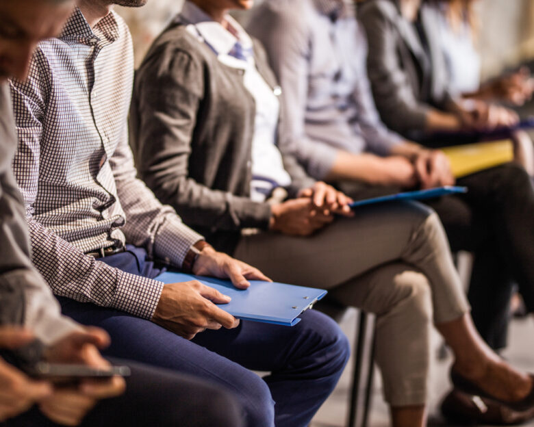 Large group of unrecognizable business people waiting for a job interview. Focus is on man with blue clipboard.