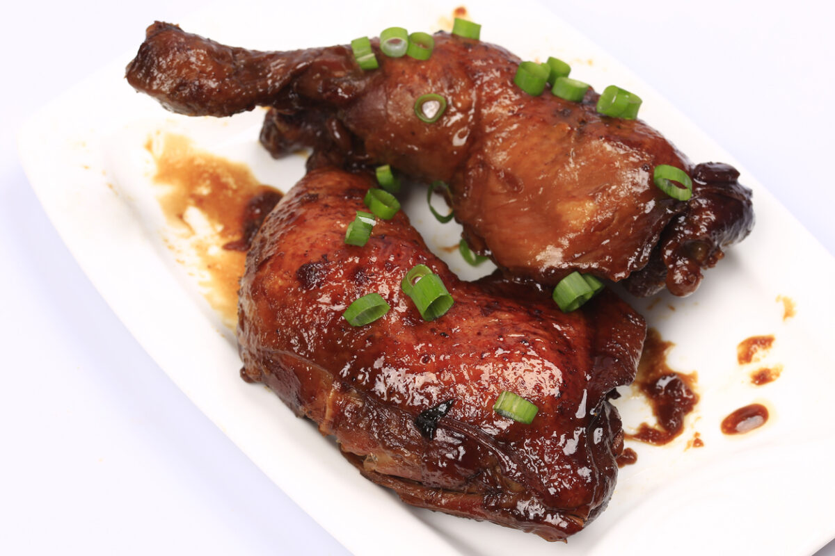 Baked chicken legs in spicy glaze with honey sauce on the plate, white background
