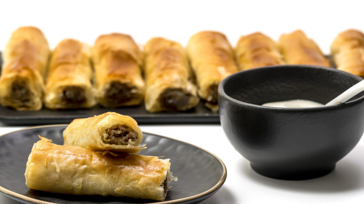 Meat rolls pastry - fried minced pork meat in spring rolls in a black oval plate, isolated on white background with stacks of rolls. Selective focus