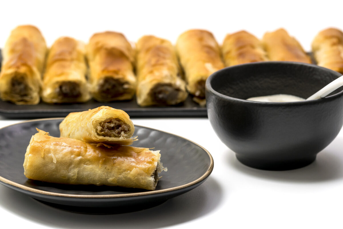 Meat rolls pastry - fried minced pork meat in spring rolls in a black oval plate, isolated on white background with stacks of rolls. Selective focus