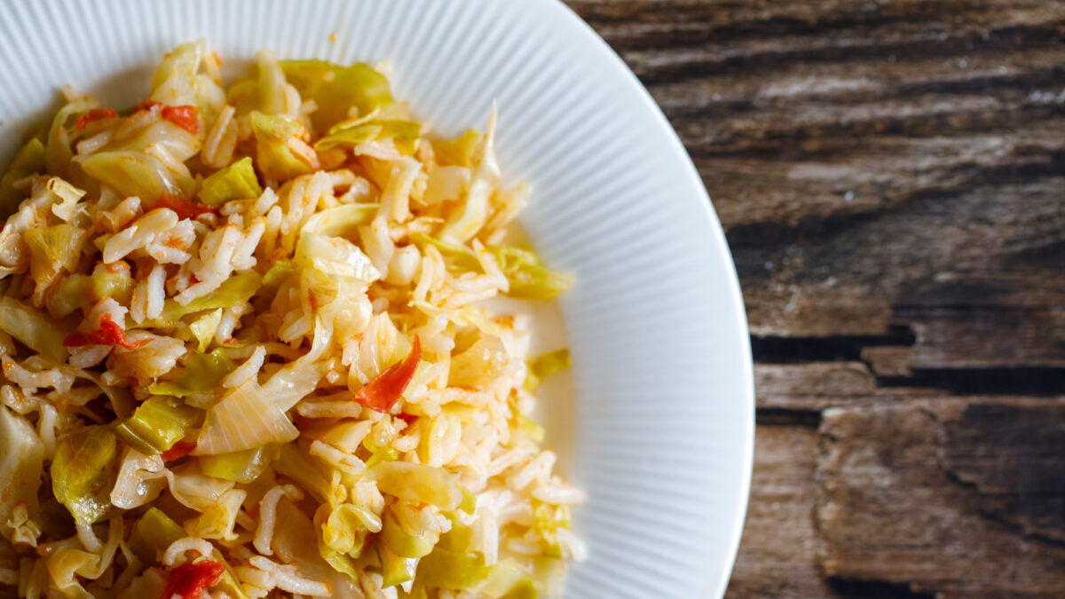 Traditional homemade Mediterranean Crete cuisine rice with vegetables cabbage, onion and tomato on white plate on old wooden table. Vegetarian healthy lunch or dinner idea. Top view