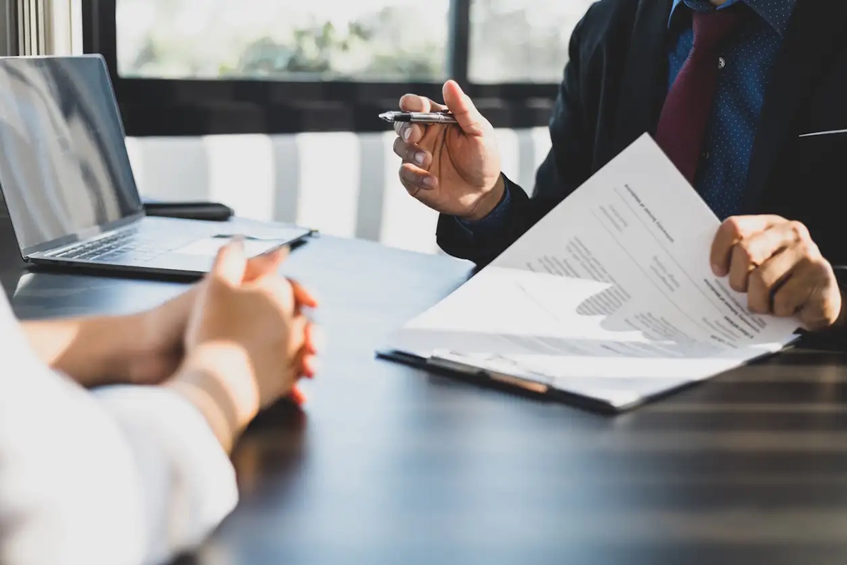 Businessman in suit in his office showing an insurance policy and pointing with a pen where the policyholder must to sign. Insurance agent presentation and consulting insurance detail to customer