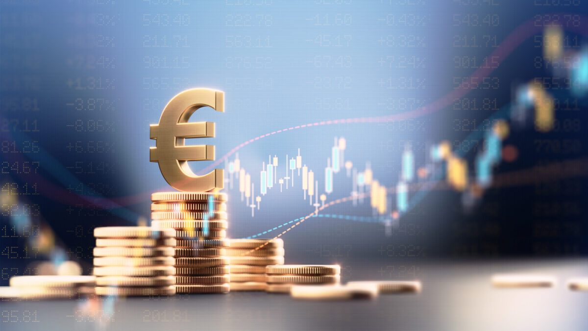 Euro symbol on top of coin stacks before blue financial graph. Horizontal composition with copy space. Business and finance concept.
