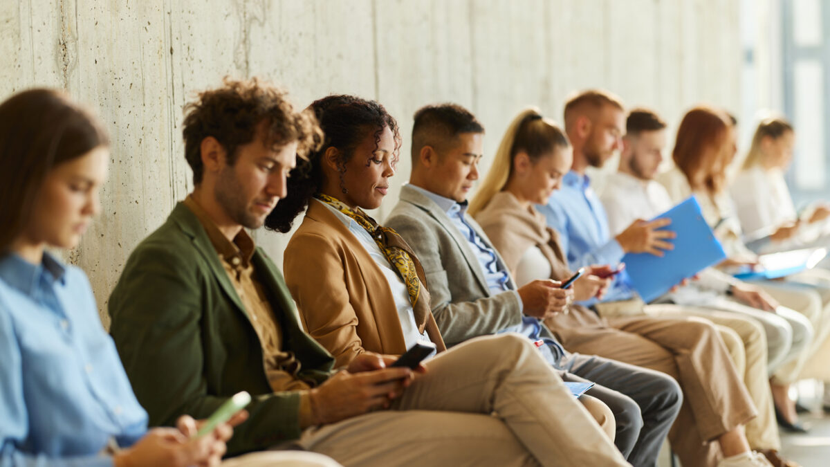 Large group of business people waiting for a job interview in a hallway. Focus is on black woman using mobile phone.