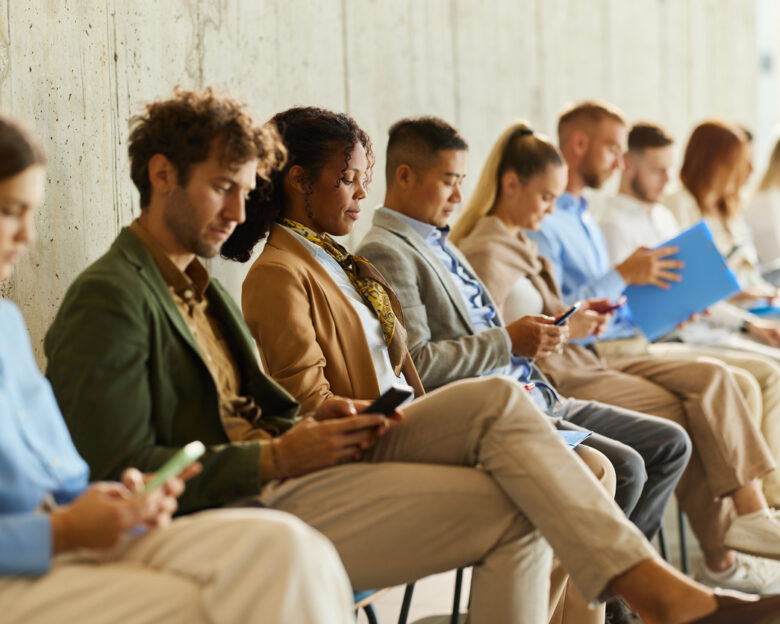 Large group of business people waiting for a job interview in a hallway. Focus is on black woman using mobile phone.
