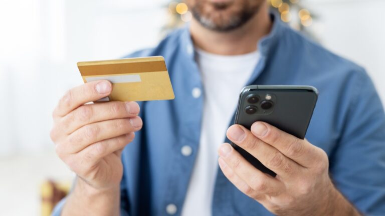 Close-up photo of young male hands holding a credit card and a mobile phone.