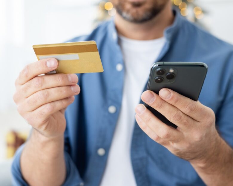 Close-up photo of young male hands holding a credit card and a mobile phone.