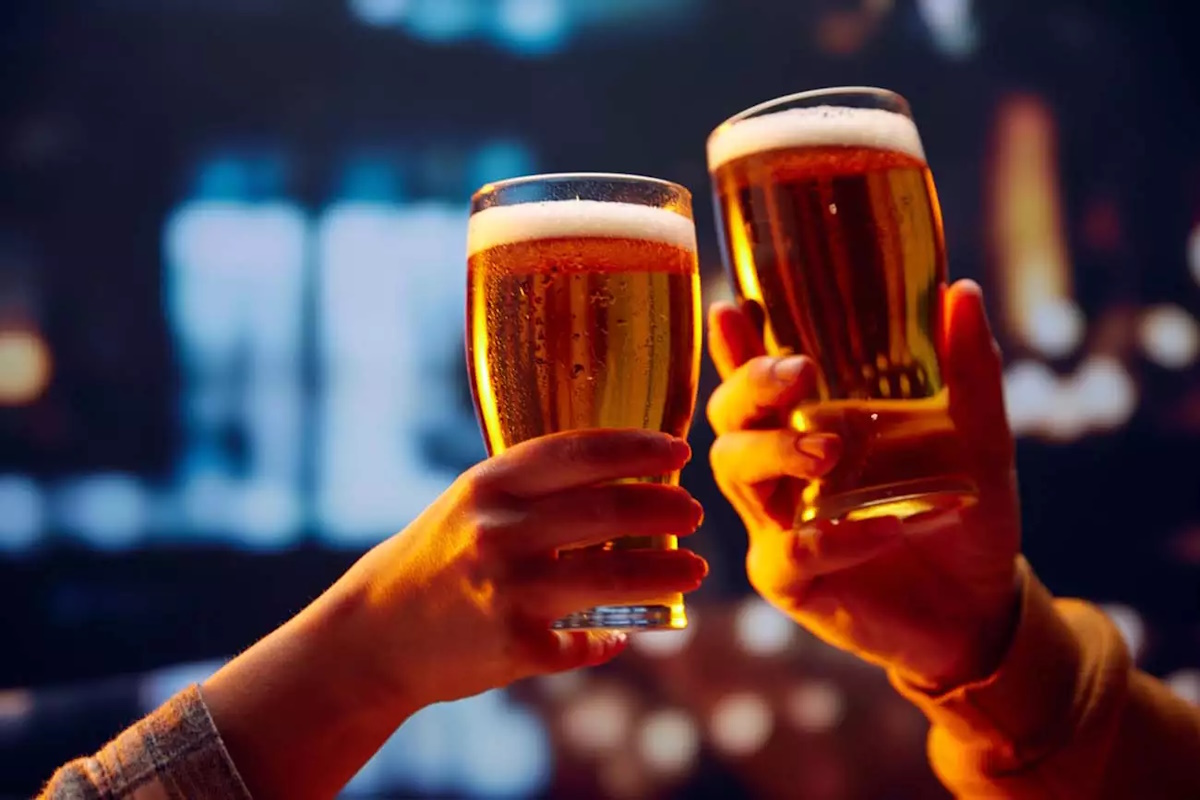 Hands holding lager light foamy big beer glasses and clinking. Two friends sitting in bar and drinking alcohol drinks. Concept of Beer Fest, party, celebration, taste, national traditions.