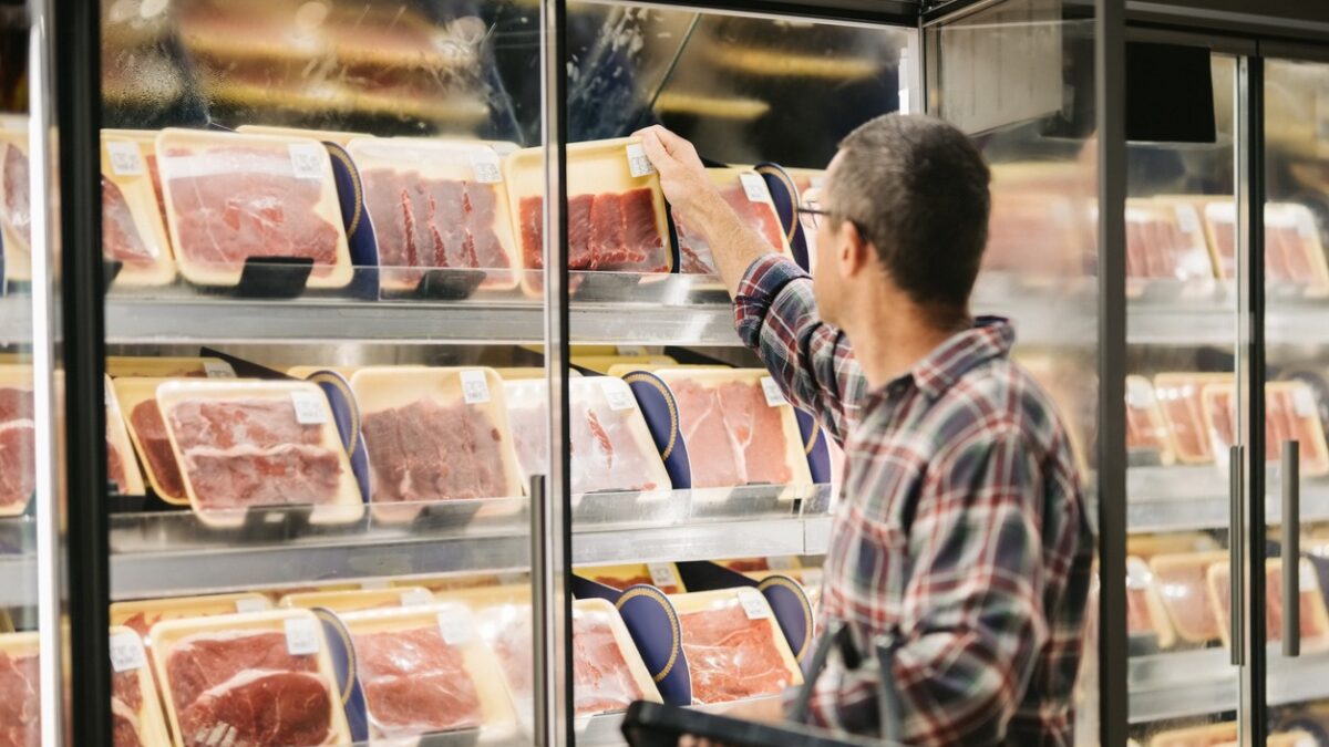 ale customer with a shopping basket taking meat from a fridge at local supermarket