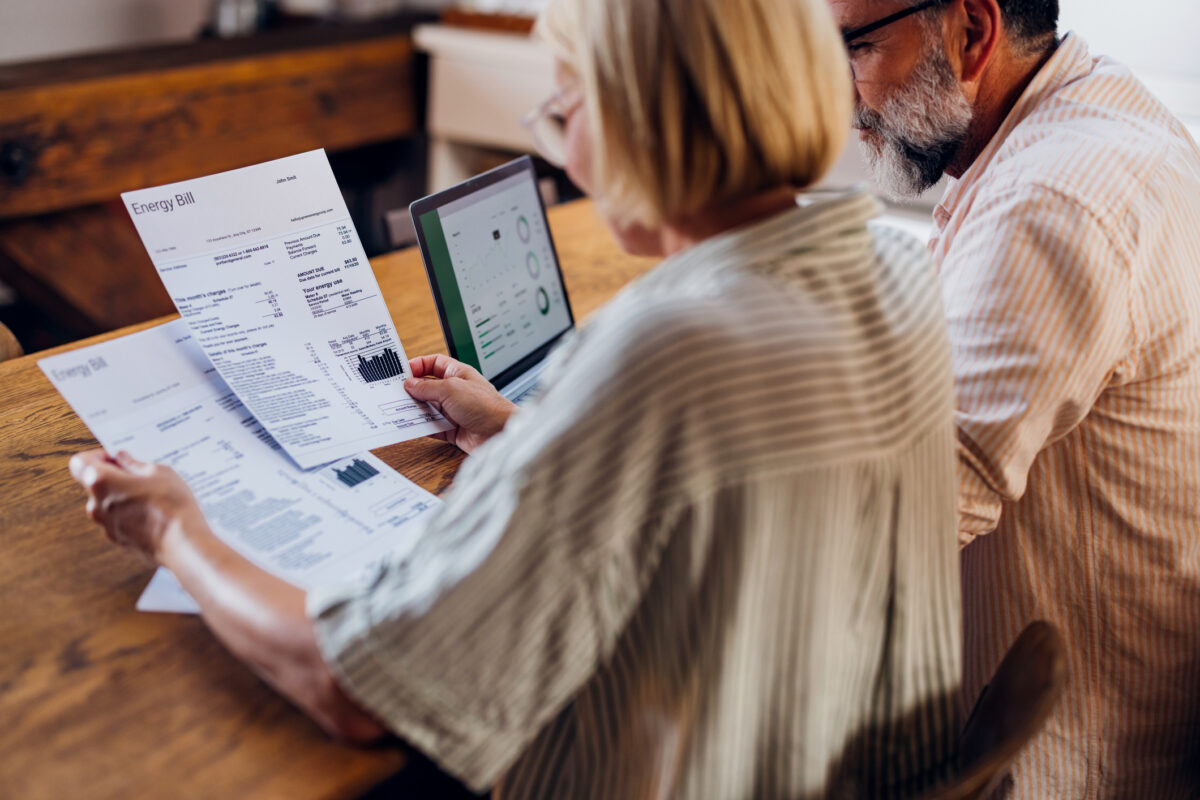 Senior couple carefully reviewing their household energy bill together on a laptop at home. They seem focused and concerned