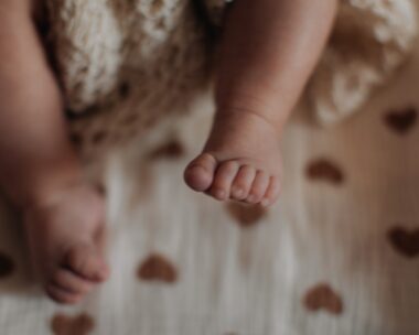 Sweet little feet of newborn baby on beige background, baby care and parenthood concept