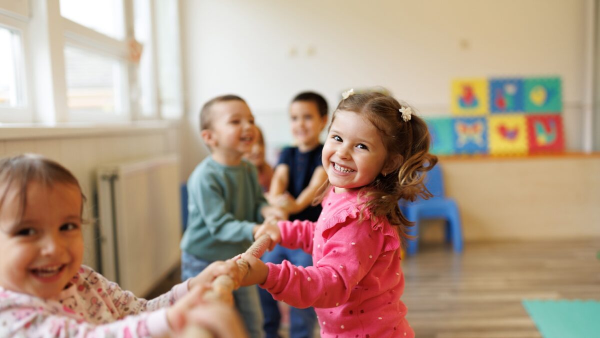 Happy group of kids playing a game of tug of war in playroom