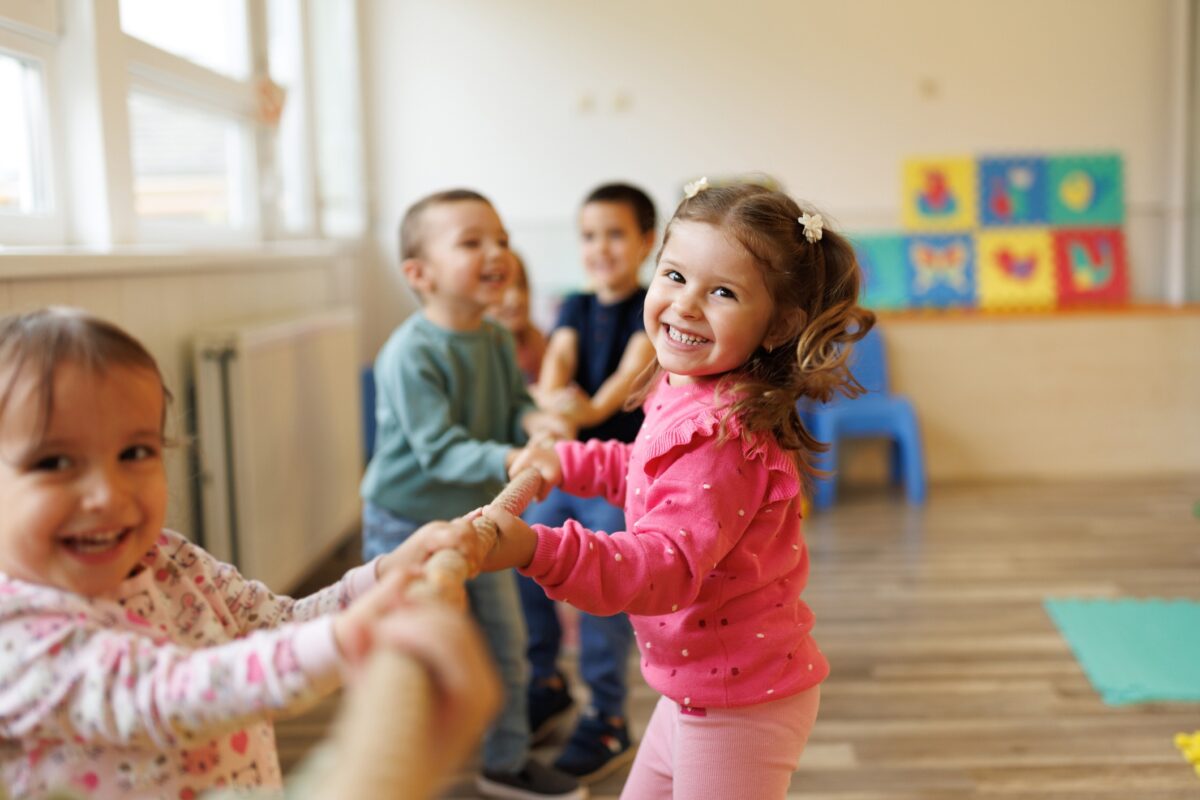 Happy group of kids playing a game of tug of war in playroom