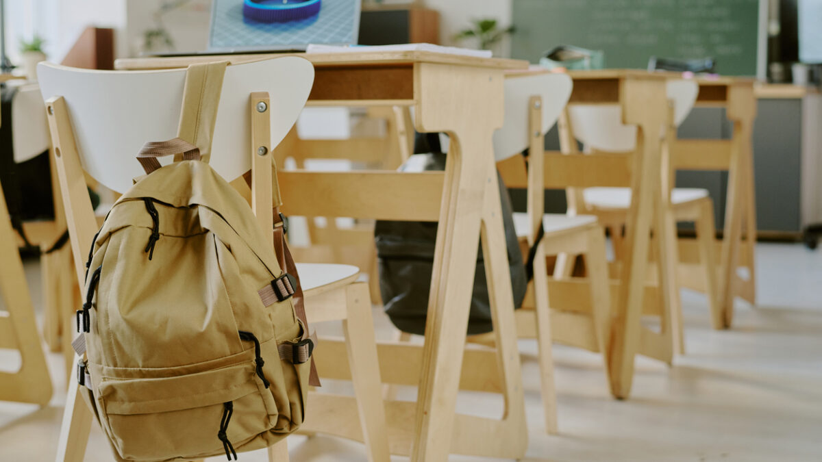 Interior of classroom showing empty chairs and desks, with backpack on back of one chair, suggesting absence of students or lesson in progress