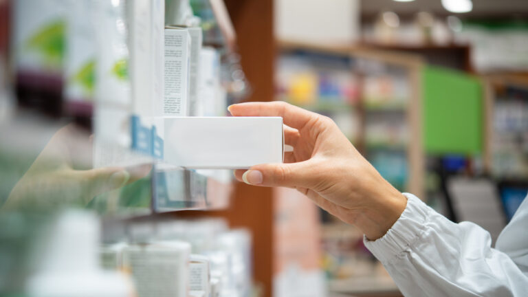 Pharmacist taking medicine box from shelf in a pharmacy