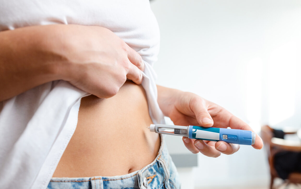 Image of an individual injecting insulin into their abdomen using a pen device. Demonstrates healthcare, diabetes management, and medication administration domestically, conveying a sense of responsibility and self-care.