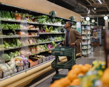A man selects vegetables in a grocery store, emphasizing healthy choices and fresh produce. The scene is well-lit and organized, showing an extensive selection of greens and other vegetables