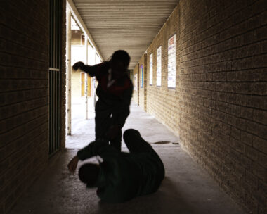 Two school kids fight in a dark passageway of their school, almost silhouette.