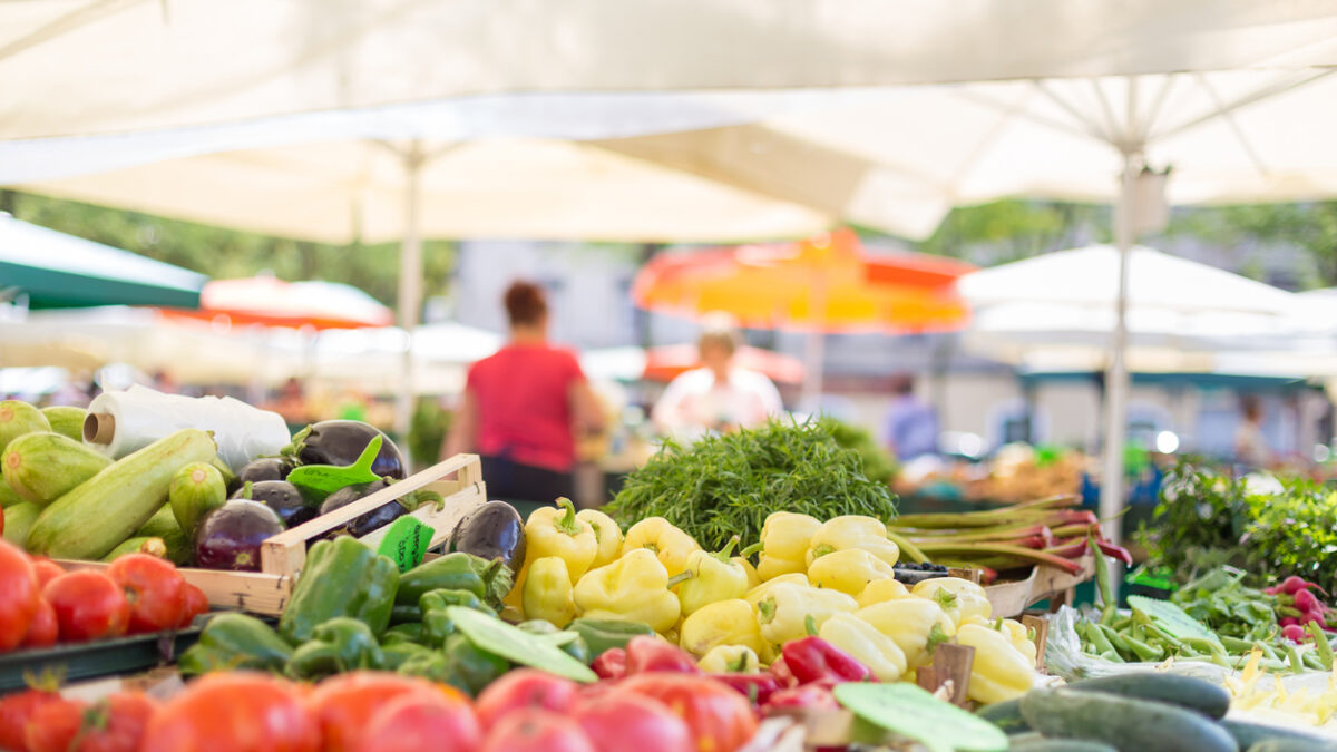 Farmers' food market stall with variety of organic vegetable. Vendor serving and chating with customers