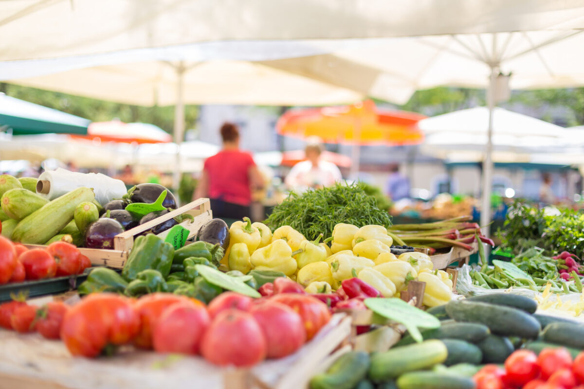 Farmers' food market stall with variety of organic vegetable. Vendor serving and chating with customers
