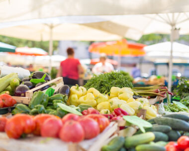 Farmers' food market stall with variety of organic vegetable. Vendor serving and chating with customers