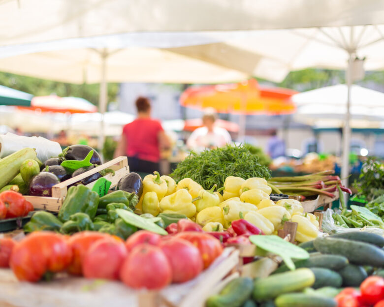 Farmers' food market stall with variety of organic vegetable. Vendor serving and chating with customers