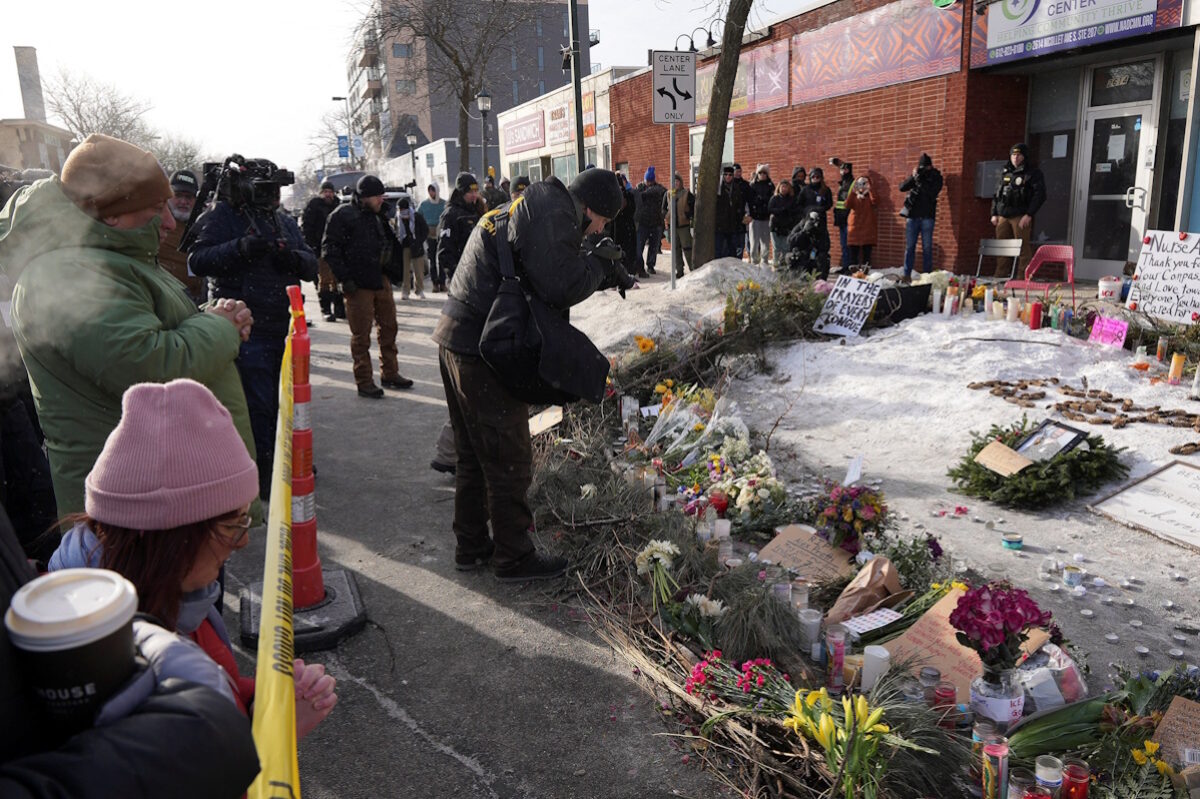 Στέλεχος του Γραφείου Ποινικής Σύλληψης (BCA) επιμελείται το σημείο όπου ο Alex Pretti, σκοτώθηκε από πυροβολισμούς ομοσπονδιακών υπαλλήλων της υπηρεσίας μετανάστευσης που προσπάθησαν να τον συλλάβουν, ενώ άνθρωποι συγκεντρώνονται σε ένα αυτοσχέδιο μνημείο, στο Μινεάπολις