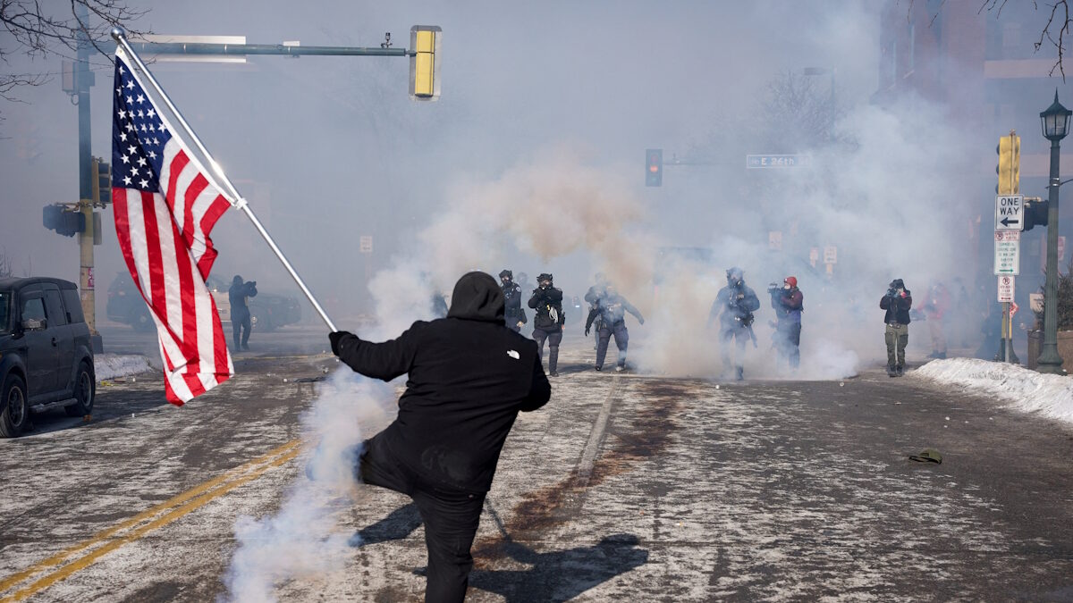 Ένα άτομο κρατά μια αμερικανική σημαία κατά τη διάρκεια συγκρούσεων μεταξύ ομοσπονδιακών πρακτόρων και μελών της κοινότητας στο σημείο όπου ομοσπονδιακοί πράκτορες πυροβόλησαν θανάσιμα έναν άνδρα ενώ προσπαθούσαν να τον συλλάβουν, στη Μινεάπολη της Μινεσότα