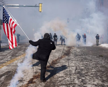 Ένα άτομο κρατά μια αμερικανική σημαία κατά τη διάρκεια συγκρούσεων μεταξύ ομοσπονδιακών πρακτόρων και μελών της κοινότητας στο σημείο όπου ομοσπονδιακοί πράκτορες πυροβόλησαν θανάσιμα έναν άνδρα ενώ προσπαθούσαν να τον συλλάβουν, στη Μινεάπολη της Μινεσότα