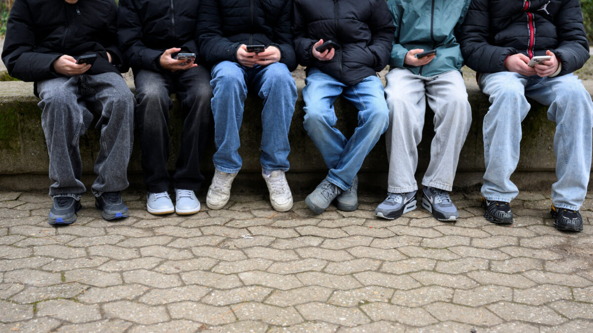 Teenagers pose for a picture while looking at their phones, in Bonn, Germany, February 20, 2026. REUTERS/Jana Rodenbusch