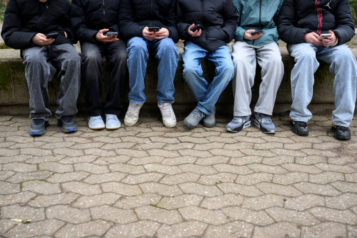 Teenagers pose for a picture while looking at their phones, in Bonn, Germany, February 20, 2026. REUTERS/Jana Rodenbusch