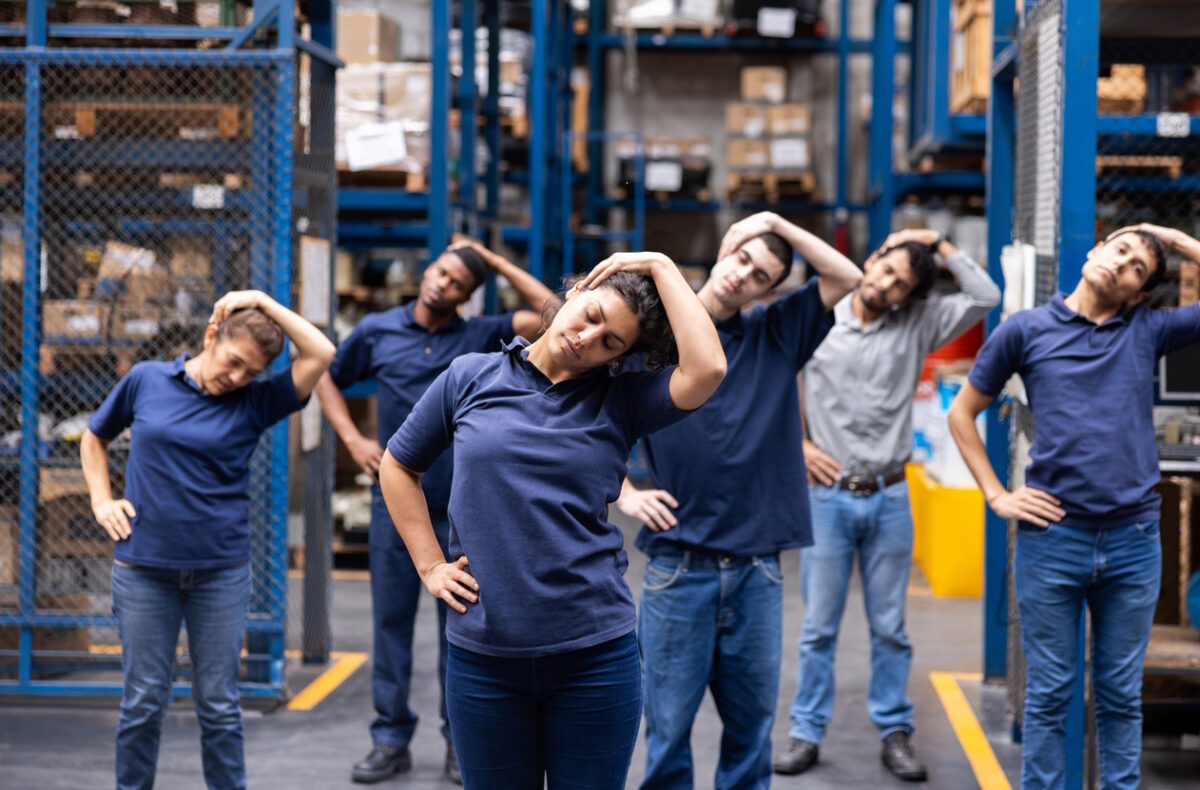 Group of Latin American workers stretching at a warehouse while having a meeting - healthy lifestyle concepts