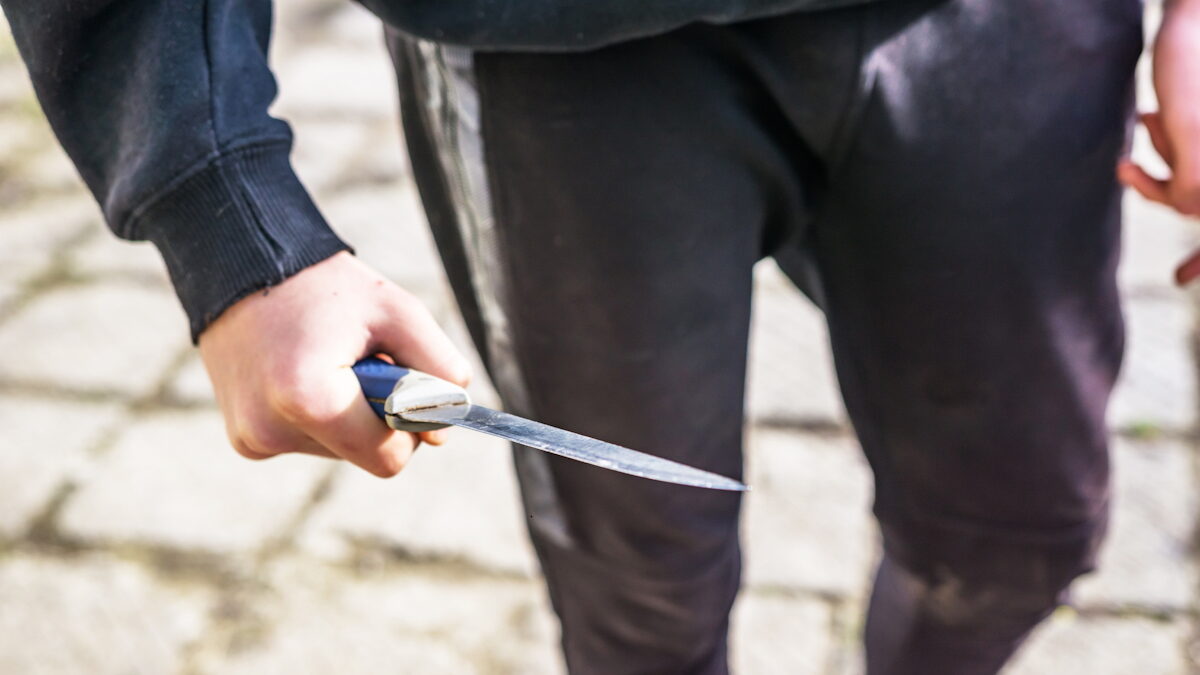 Close-up of a young man's hand with a knife, a big blade. Arrogance and violence among young people. Shallow depth of focus.
