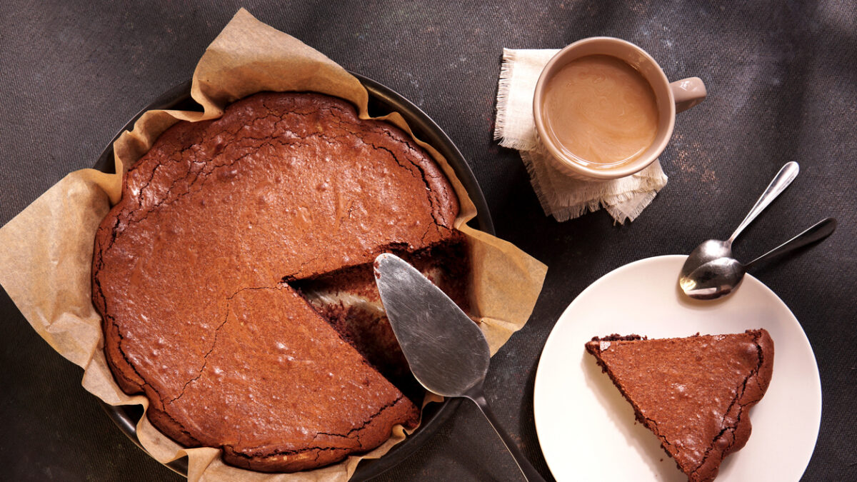 Homemade dark chocolate cake brownie in baking pan, mug with tea or coffee, chocolate on dark table with window light. Delicious bitter sweet and fudge. Flat lay, top view, vintage style.