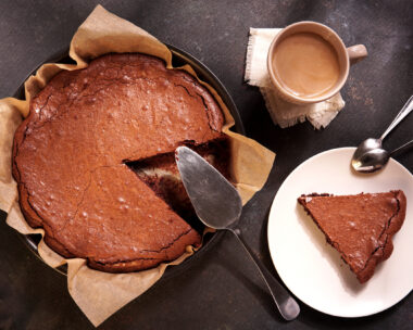 Homemade dark chocolate cake brownie in baking pan, mug with tea or coffee, chocolate on dark table with window light. Delicious bitter sweet and fudge. Flat lay, top view, vintage style.
