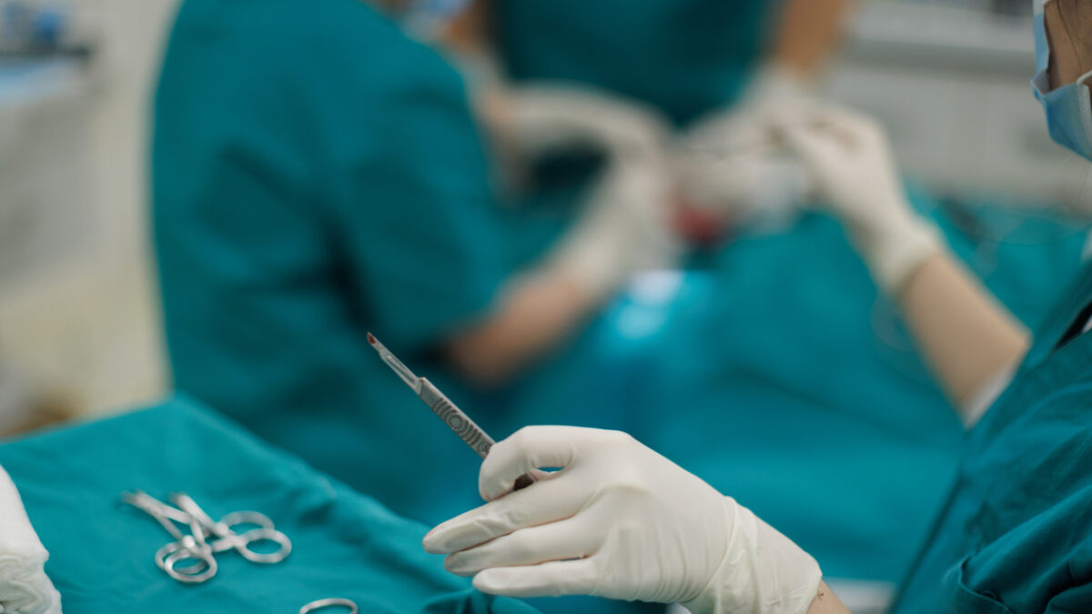 Nurse skillfully provides a scalpel to the surgeon during an ear reconstruction surgery. The precision and efficiency of the surgical team reflect the complexity and care required for this reconstructive procedure.
