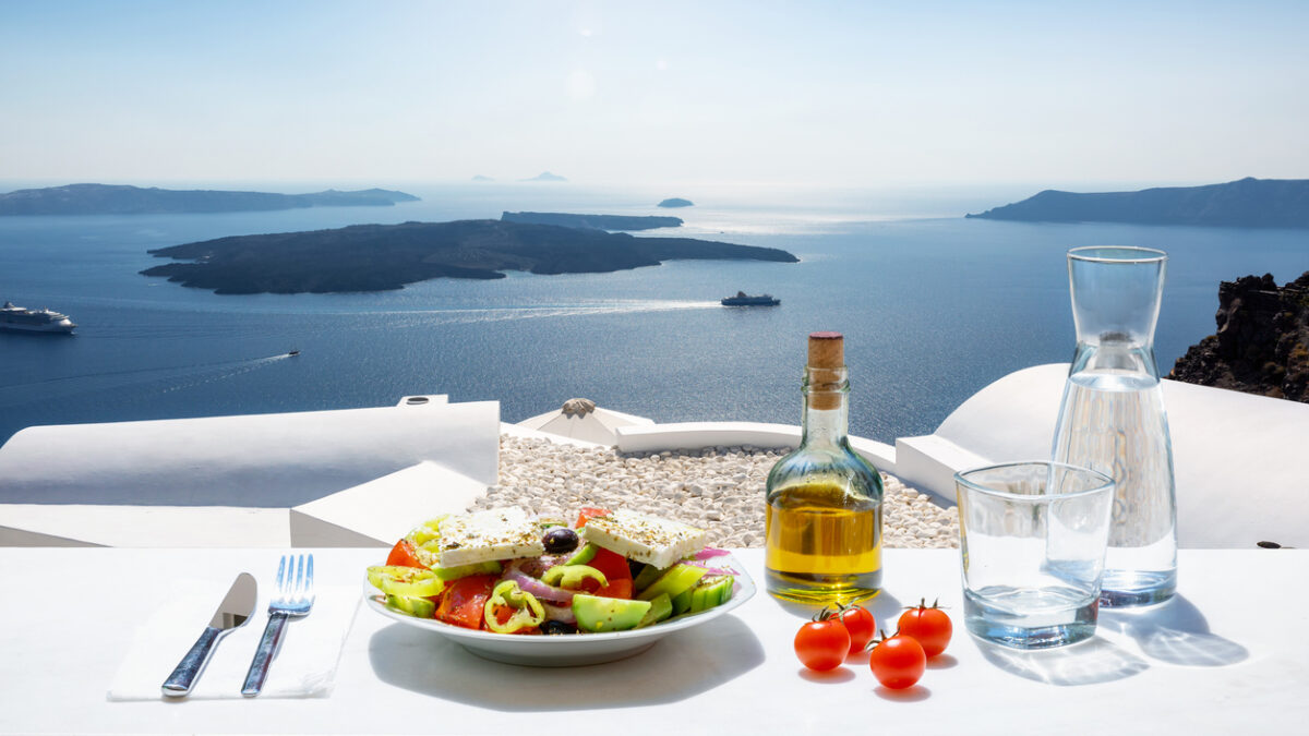 A Greek salad with olive oil and tomatoes in front of the a breathtaking view to the blue, Aegean sea as a concept of Greek food in summer time