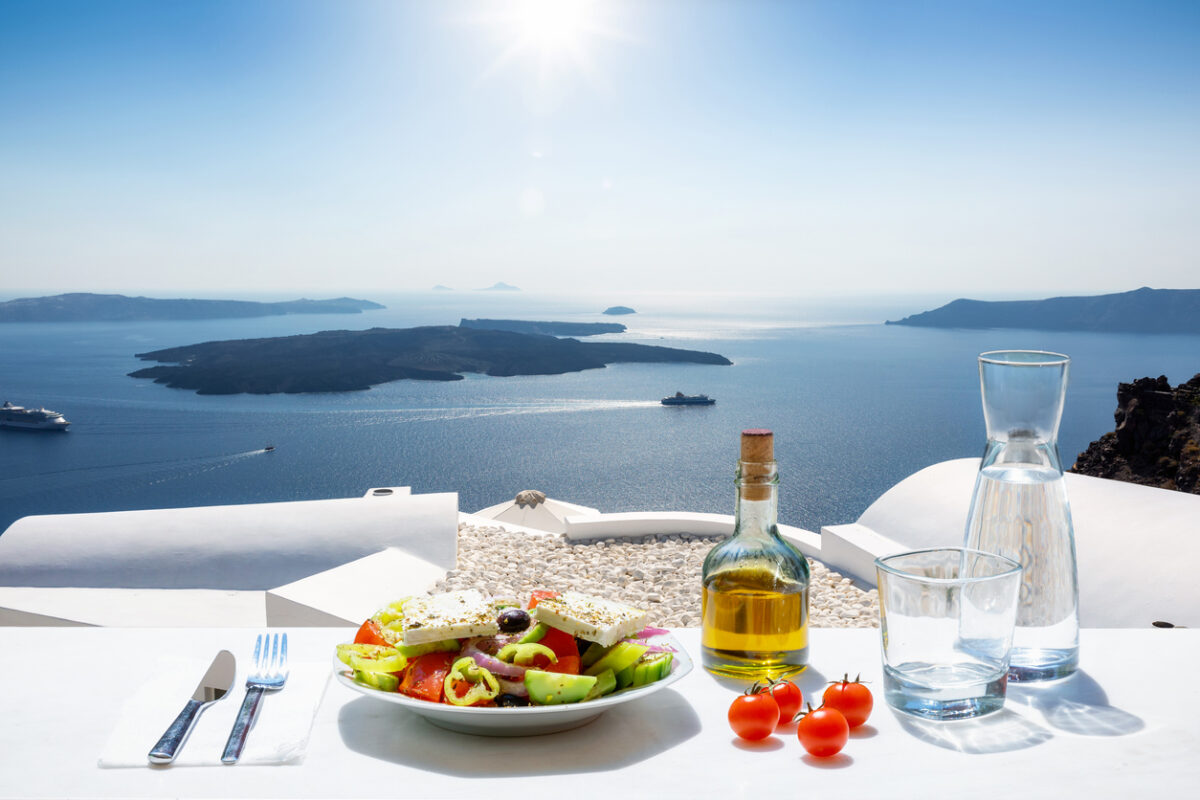 A Greek salad with olive oil and tomatoes in front of the a breathtaking view to the blue, Aegean sea as a concept of Greek food in summer time
