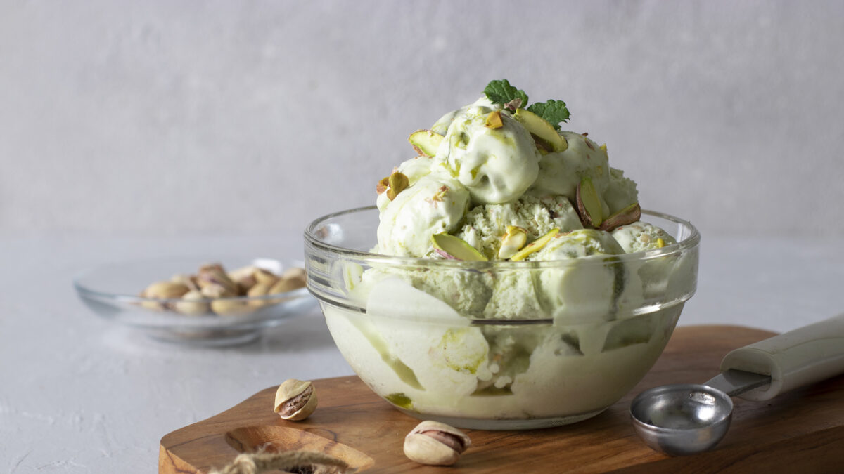 Pistachio ice cream with nuts in transparent glass ice-cream bowl on a light gray background.