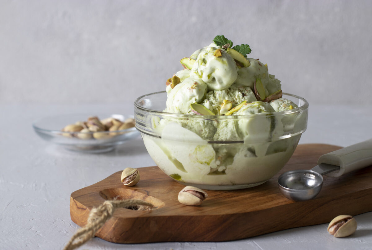 Pistachio ice cream with nuts in transparent glass ice-cream bowl on a light gray background.