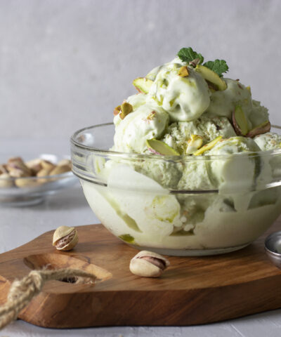 Pistachio ice cream with nuts in transparent glass ice-cream bowl on a light gray background.