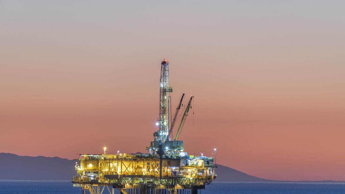 Dramatic image of an offshore oil platform off the coast of California against a pink winter sky as the sun sets and the rig's lights illuminate.