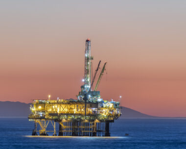 Dramatic image of an offshore oil platform off the coast of California against a pink winter sky as the sun sets and the rig's lights illuminate.