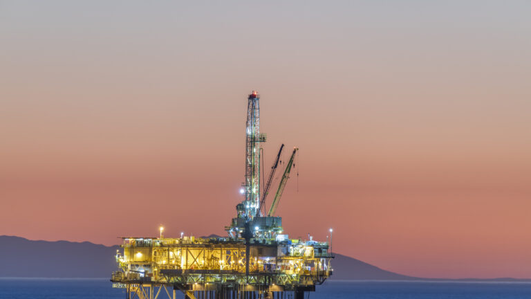 Dramatic image of an offshore oil platform off the coast of California against a pink winter sky as the sun sets and the rig's lights illuminate.