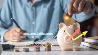 Man putting coins in piggy bank and taking notes in notebook money saving concept business