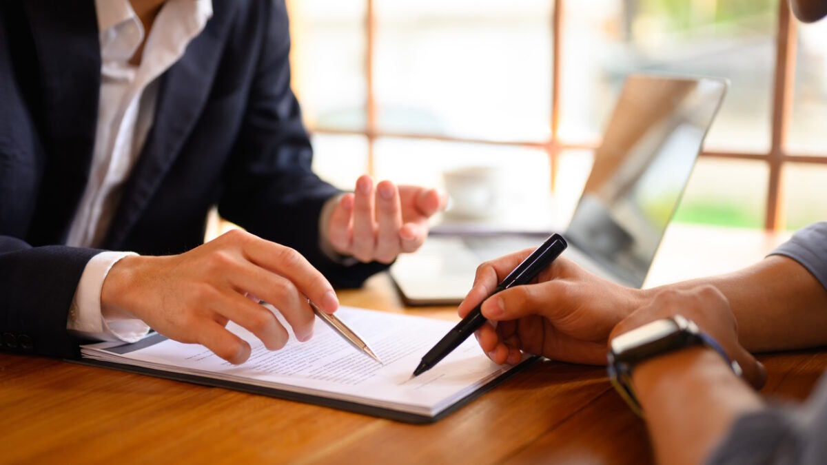 Closeup lawyer or insurance agent pointing at contract showing male client where to signature sign.