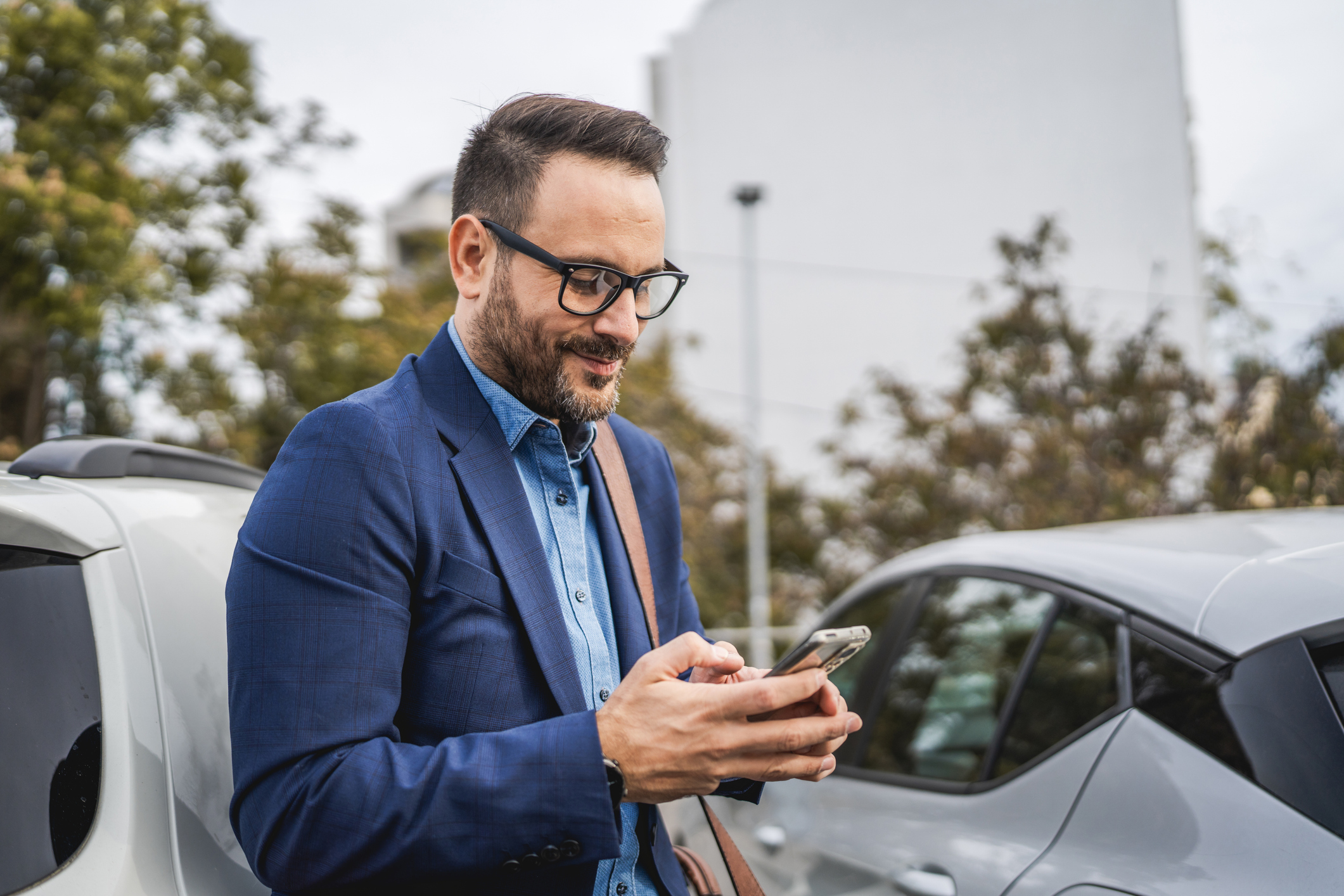 Adult smile businessman stand in the parking lot and use mobile phone