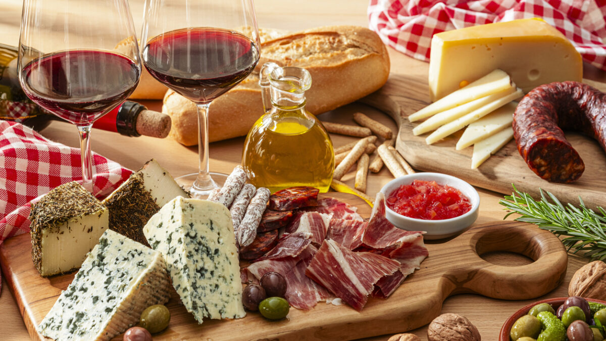 cheese and Serrano ham board, red wine and olives on wooden table